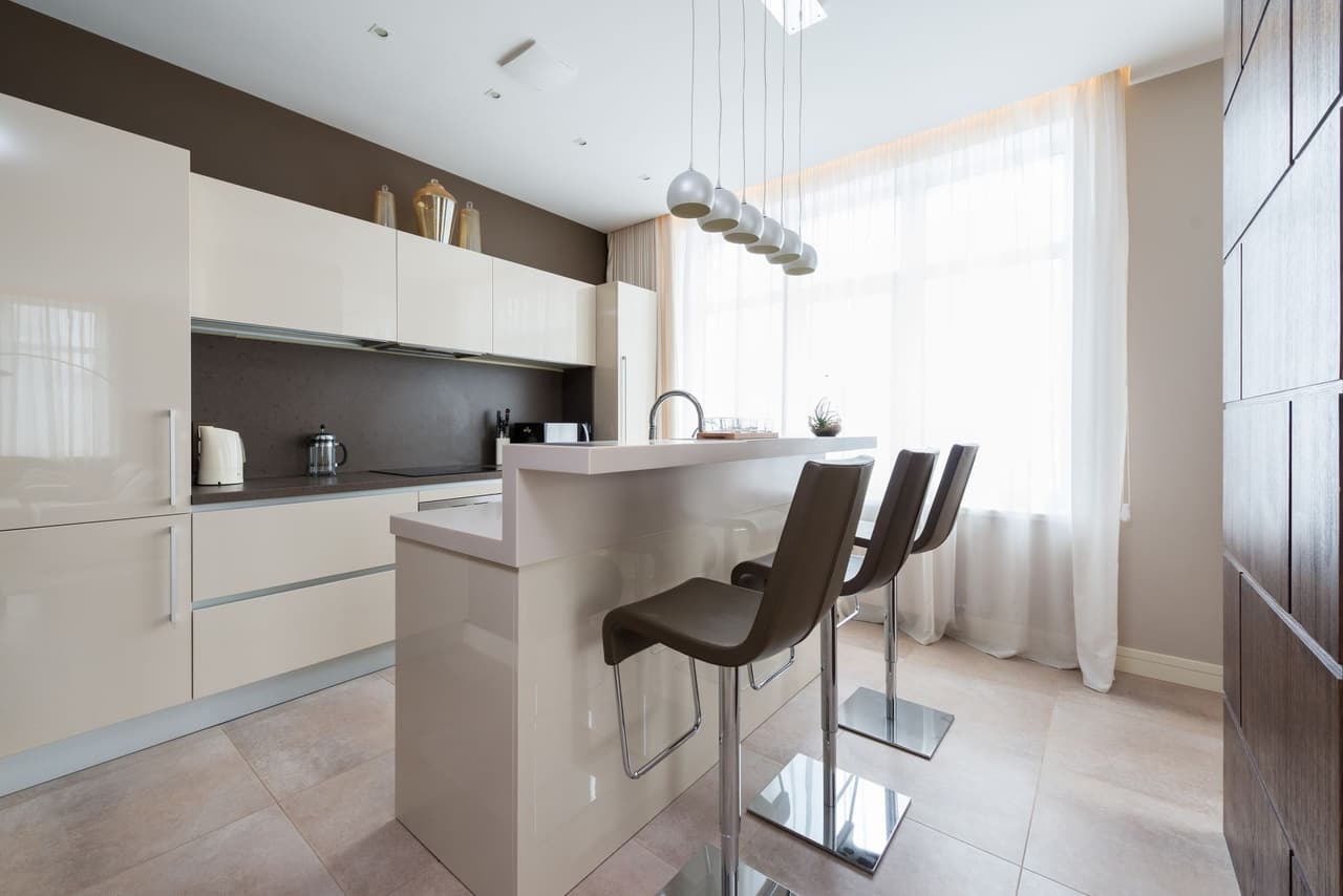 Bright kitchen with a cream island, brown leather bar stools, pendant lights and large windows with sheer curtains