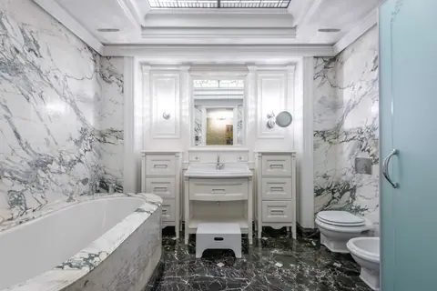 Bathroom with veined marble walls, an oval tub, a white paneled vanity and a dark marble floor